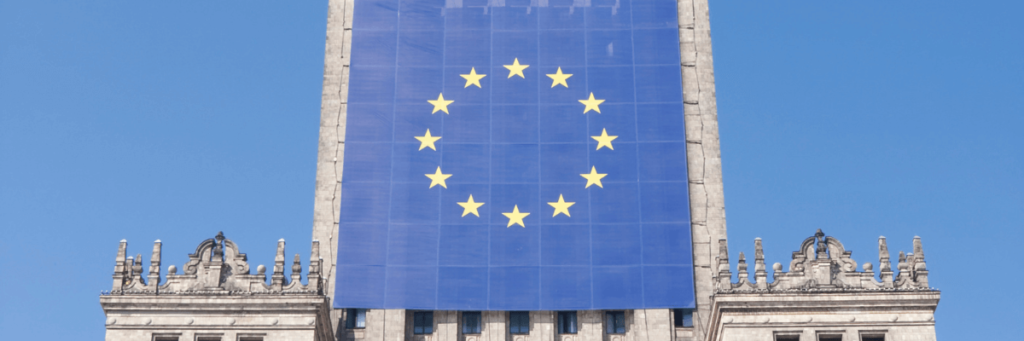 Image of the EU flag draped down an old looking building with a blue sky behind the building. This image is used by Patient Guard to describe EU Medical Device and IVD regulatory and quality assurance related content