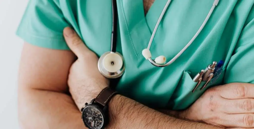 Image shows a Doctor in green scrubs with folded arms - This image is used by Patient Guard to describe its medical device and IVD regulatory and quality assurance related content.