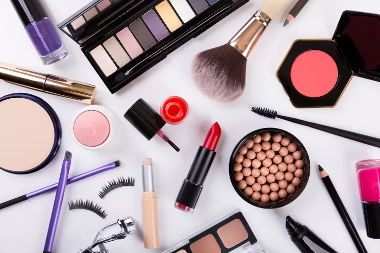 Image of colourful cosmetics on a white background including lipstick, bushes, blush, eye lashes, bronzer, eye shadows