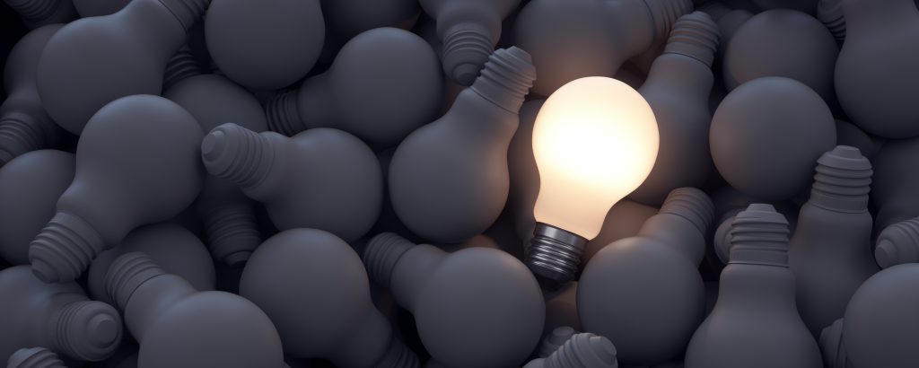Image of a pile of black old broken lightbulbs with a single lightbulb on the pile that is not broken and shining light, indicating a good idea. Helping bring your Ideas to life